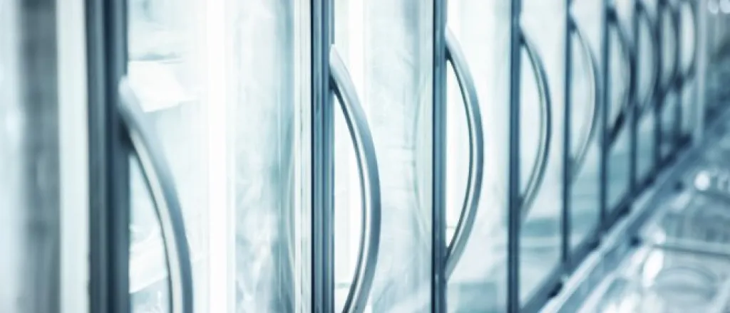 A close-up view shows a line of built-in refrigerators at a supermarket. The doors are glass, and the handles are silver.
