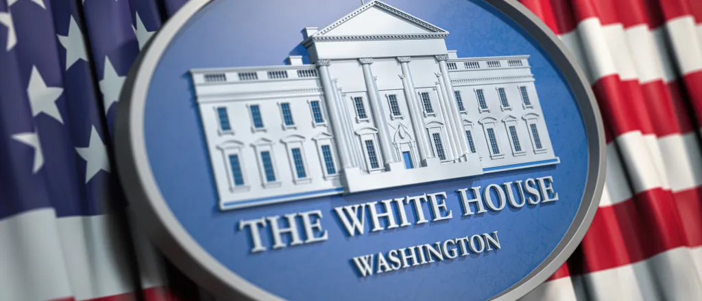 Close up of an oval, carved plaque with an image of the White House. The plaque is on top of a flag of the United States of America.