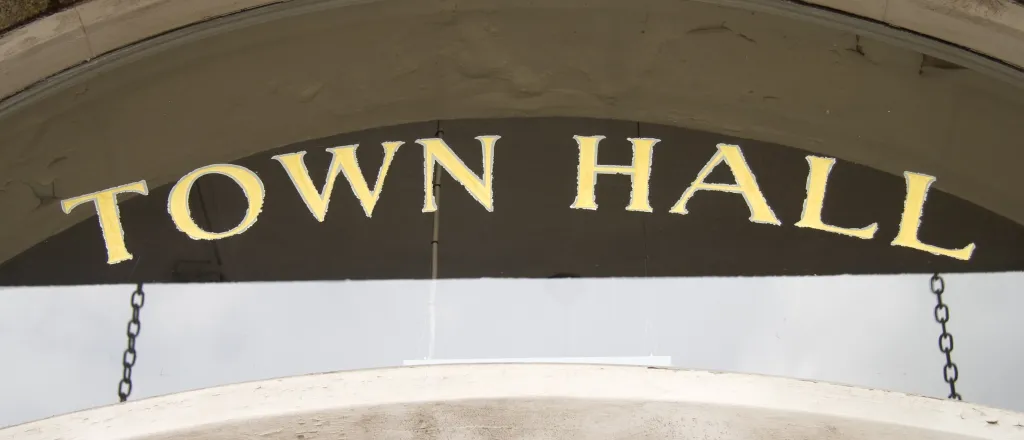 PROMO HIRES Government - Building Town Hall Politics - LanceB - iStock-92318563 Close up of a door to a building with a glass transom above. The words "Town Hall" are stenciled on the glass in gold leaf foil.