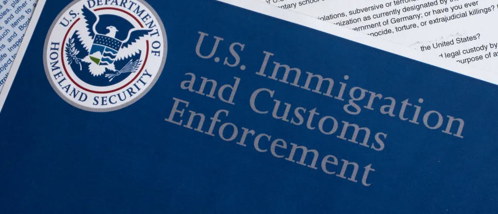 Overhead closeup of documents. The top document is entitled "U.S. Immigration and Customs Enforcement" with the United States Department of Homeland Security logo.