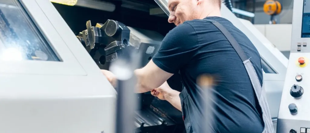 A professional tooling machine worker in a warehouse. They're smiling as they work on a tooling project inside the machine.