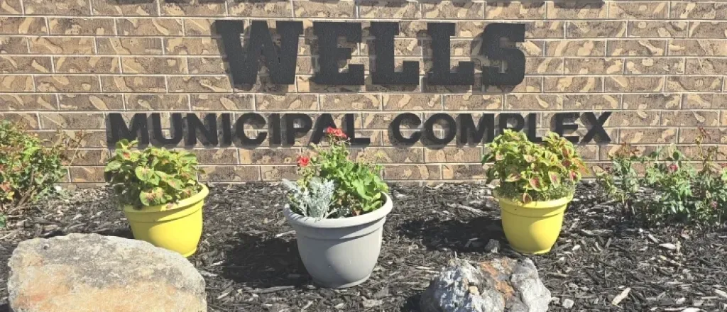 Town of Cheyenne Wells Brick wall with the words Cheyenne Wells Municipal Complex. Assorted potted plants and rocks are on mulched ground in front of the sign.