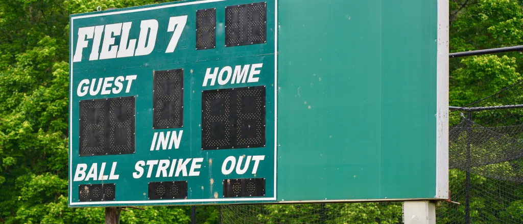 Baseball or softball scoreboard in front of trees.