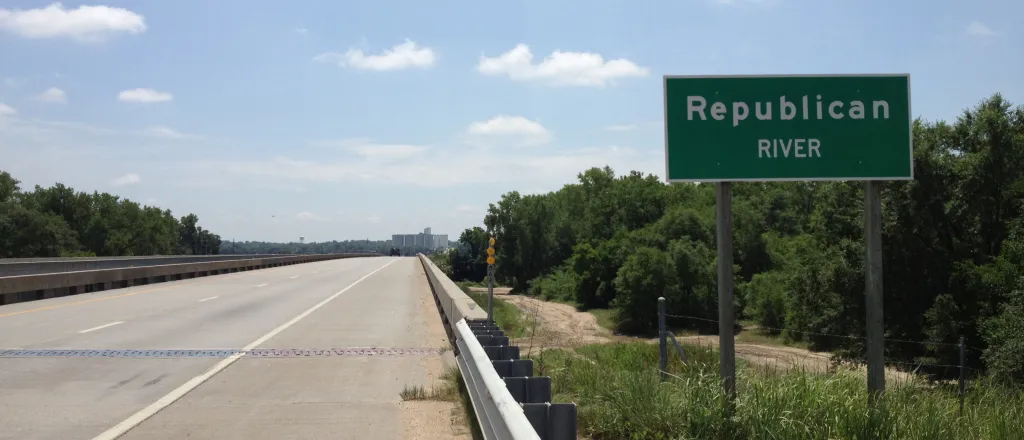 Sign with the words "Republican River" standing next to a bridge.