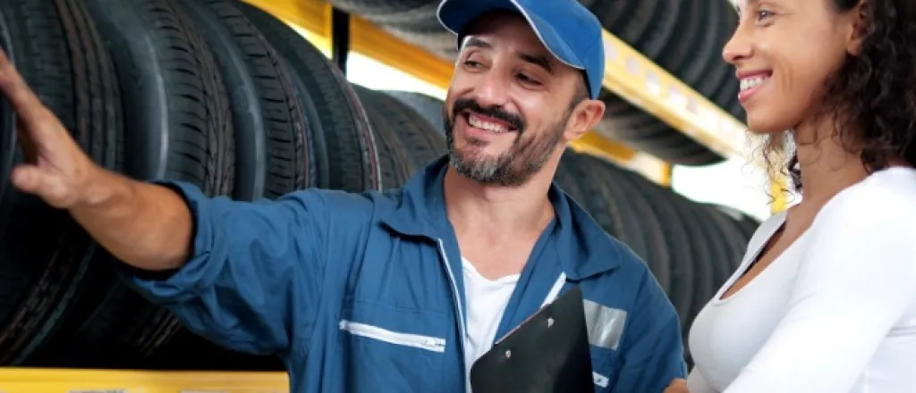 A salesman speaking with a customer about tires, while placing his hand on one option. Both people are smiling.