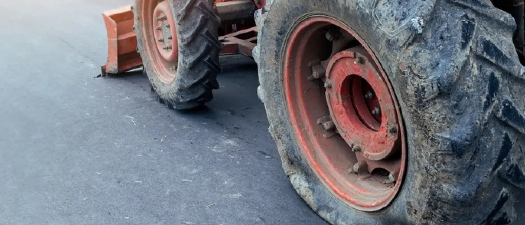 A red tractor sitting on the side of a paved road with a blown out rear tire and damaged rubber visible on the wheel.