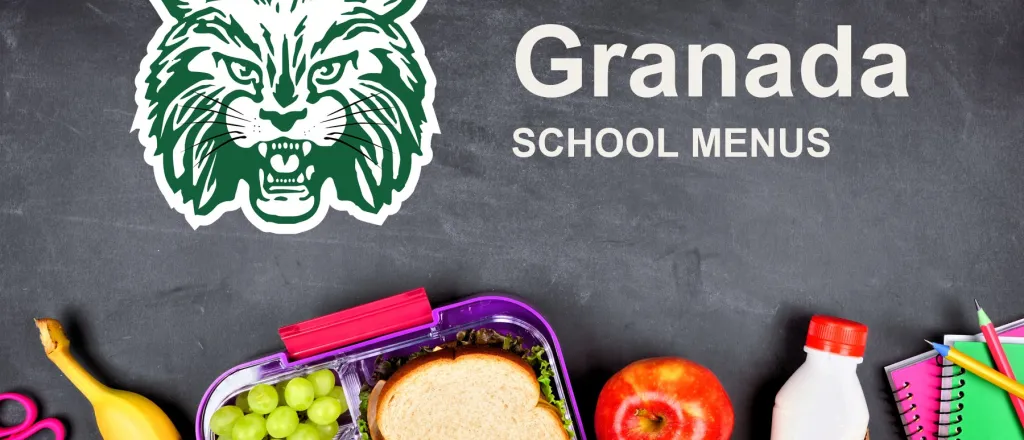 The Granada School Bobcats mascot, chalked on a blackboard above a packed school lunch of a sandwich, grapes, carrots, an apple and a bottle of milk, with pencils and notebooks. The board reads “Granada School Menus”.
