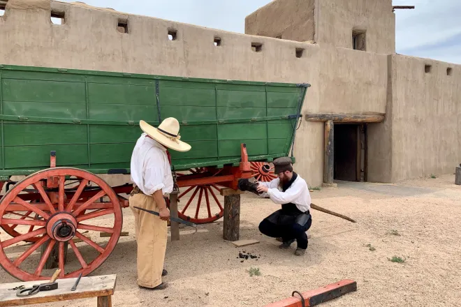 PICT Bent's Old Fort park staff greasing the axle of the park's green Conestoga Wagon. Courtesy NPS - Jake Koch