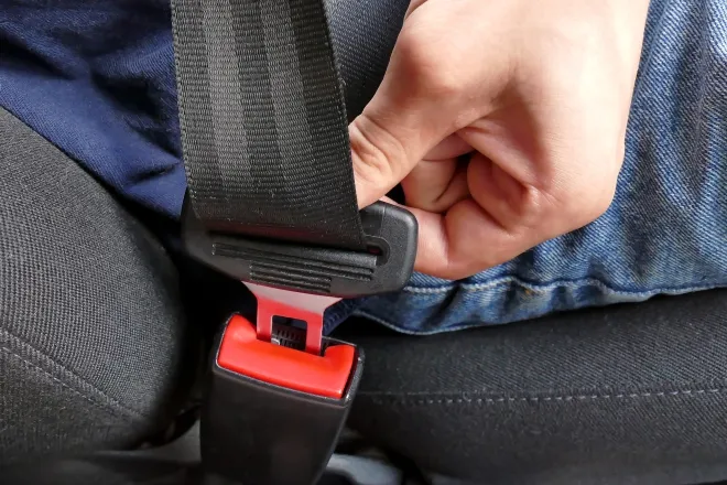 Closeup of a hand fastening a seat belt in a vehicle.