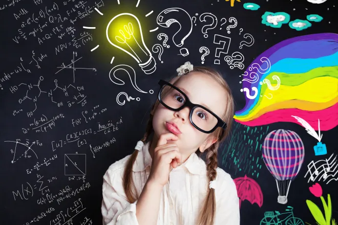 Child wearing glass with head tilted in an inquisitive pose in front of a chalkboard with colorful images