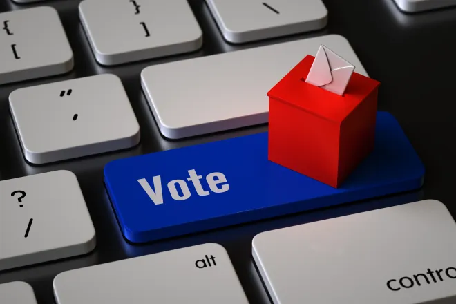 Closeup of a computer keyboard with a key labeled "Vote." A miniature ballot box is sitting on the key