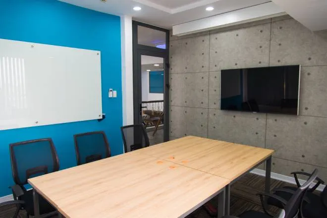 A wooden table in a conference room surrounded by black office chairs. A whiteboard hangs on a blue wall.