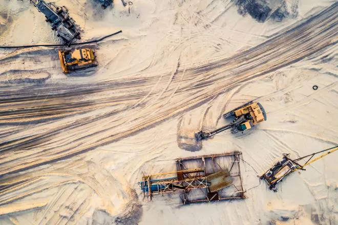 A top-down view of a sandy area with assorted industrial mining equipment sitting atop the tire-streaked sand.