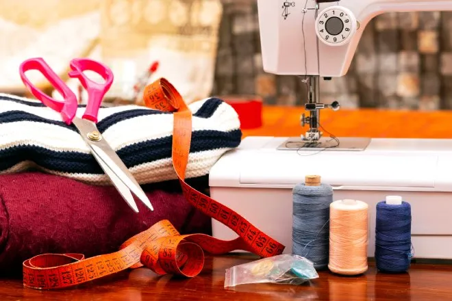 A sewing machine with a selection of notions including a tape measure, thread spools, and a variety of fabrics.