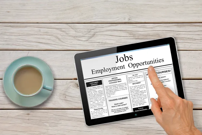 Tablet on a table next to a cup of coffee with the words "Jobs - Employment Opportunities." A hand hovers over the tablet.