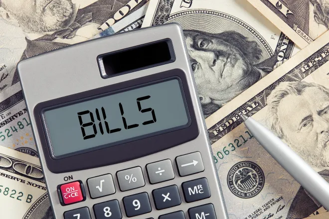 Calculator sitting on top of assorted paper money with the word "bills" displayed on the screen.