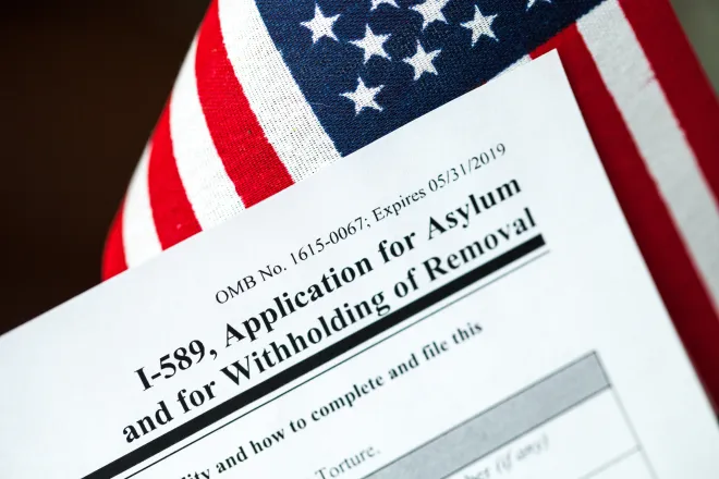 Closeup of the corner of a United States Government I-589 immigration form with a United States flag in the background.