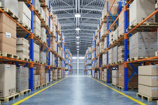  A large warehouse is organized with long rows of shelves covered in pallets and differently sized boxes.