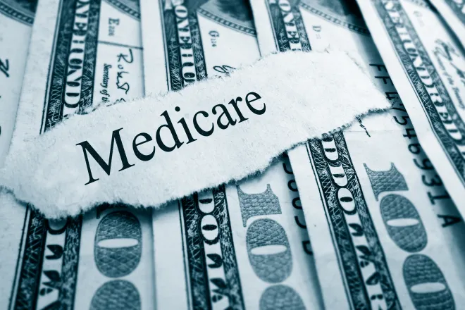 A scrap of torn paper with the word "Medicare" rests on top of a spread of United States 100 dollar currency.