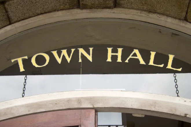 Close up of a door to a building with a glass transom above. The words "Town Hall" are stenciled on the glass in gold leaf foil.