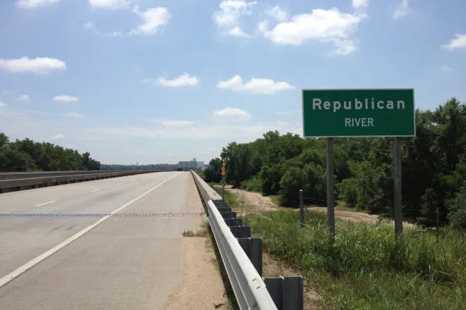 Sign with the words "Republican River" standing next to a bridge.