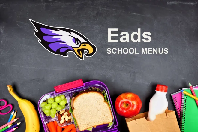 The Eads School Eagles mascot, chalked on a blackboard above a packed school lunch of a sandwich, grapes, carrots, an apple and a bottle of milk, with pencils and notebooks. The board reads “Eads School Menus”.