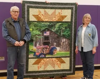 Man and woman standing on either side of a quilt.