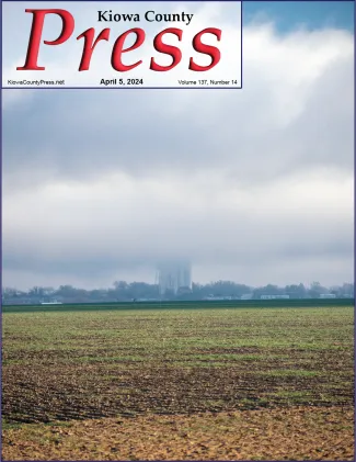 Clouds and fog partly obscuring a small town and grain elevator with a field of sprouting wheat the the foreground.