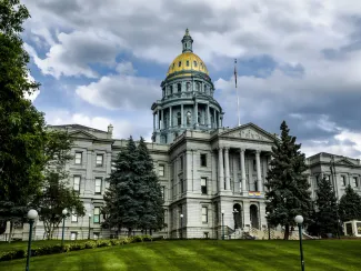 Colorado State Capitol Building fronted by green trees under a cloudy sky