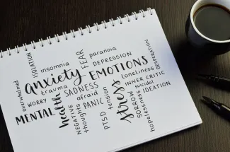 Note pad on a table with numerous descriptive words about mental health next to a cup of coffee