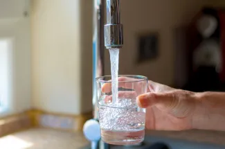 Hand filling a glass with water from a faucet.