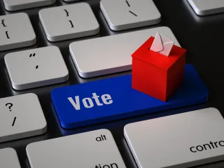 Closeup of a computer keyboard with a key labeled "Vote." A miniature ballot box is sitting on the key
