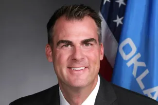 Oklahoma Governor Kevin Stitt posing in front of the Oklahoma state flag