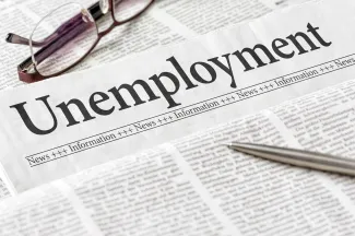 Section of a newspaper headlined "Unemployment" with a pen and pair of glasses