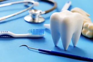 Replica human tooth surrounded by dental instruments and a stethoscope.