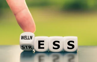 PROMO HIRES Health - Wellness Stress Blocks Words Mental Behavioral - iStock - Fokusiert Dice with a finger tipping one to change the word from "Stress" to "Wellness"