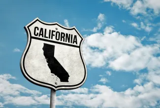 Road sign with the word "California" and a silhouette of the state. A cloudy sky is in the background.