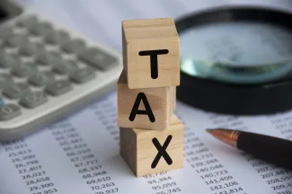 Tax word on wooden blocks with calculator, pen, magnifying glass and data analysis background.