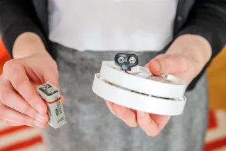 Person holding a smoke alarm or carbon monoxide alarm to change the battery.