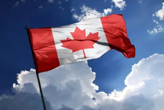 Flag of Canada against a partly cloudy, sunlit sky