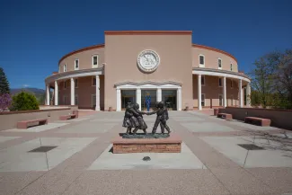 PROMO HIRES Building - Government New Mexico State Capitol - jdwfoto - iStock-1487999298 Entrance to the New Mexico State Capitol building. A statue of people is in a plaza area in front of the building.