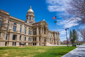 PROMO HIRES Building - Government Wyoming State Capitol - Cheri Alguire - iStock-1512457343 View of the Wyoming State Capitol Building from an angle. A flagpole with the United States and Wyoming flags is in front.