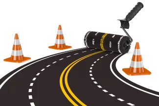 PROMO HIRES CROPPED Transportation - Road Construction Cone Zone - ISerg - iStock-1333705544 Concept image of a paint roller creating a four-lane road. Construction cones are at the sides.