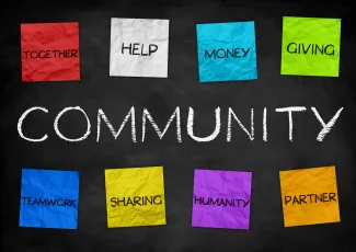 PROMO HIRES Community - Color Paper Words - iStock Word "Community" written on a chalkboard, with eight colored paper notes above and below reading "togetherness, help, money, giving, teamwork, sharing, humanity, and partner"