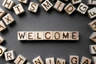 PROMO HIRES Community - Words Welcome Blocks Living - iStock - Roman Didkivskyi Assorted wooden blocks with letters on the side, surrounding wooden blocks spelling the word "welcome"