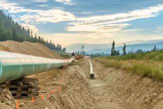 PROMO HIRES Construction Pipe Pipeline Energy - vadimgouida - iStock-1424680550 Trench in dirt with a segment of pipe, and another segment sitting above awaiting placement