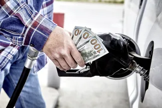 PROMO HIRES Energy - Gasoline pump fuel money cash transportation - iStock - wingedwolf Close up of a person's hand on a gas dispenser nozzle clutching three United States one hundred dollar bills.