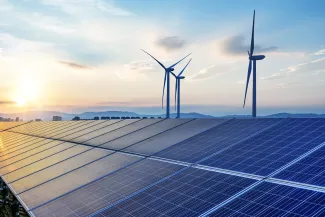 PROMO HIRES Energy - Solar Panels Wind Turbines Sky Clouds. iStock - hrul Solar panels with wind turbines in the background.