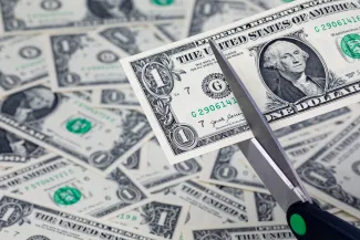 PROMO HIRES Finance - Budget Cut Money Currency Scissors - JJ Gouin - iStock-1642293566 A pair of scissors is preparing to cut a United States one dollar note. In the background, additional dollar bills are strewn haphazardly.