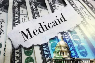 PROMO HIRES Finance - Government Medicaid Words Budget Money Cash - zimmytws - iStock-2206705589 A scrap of torn paper with the word "Medicaid" rests on top of a spread of United States 100 dollar currency.